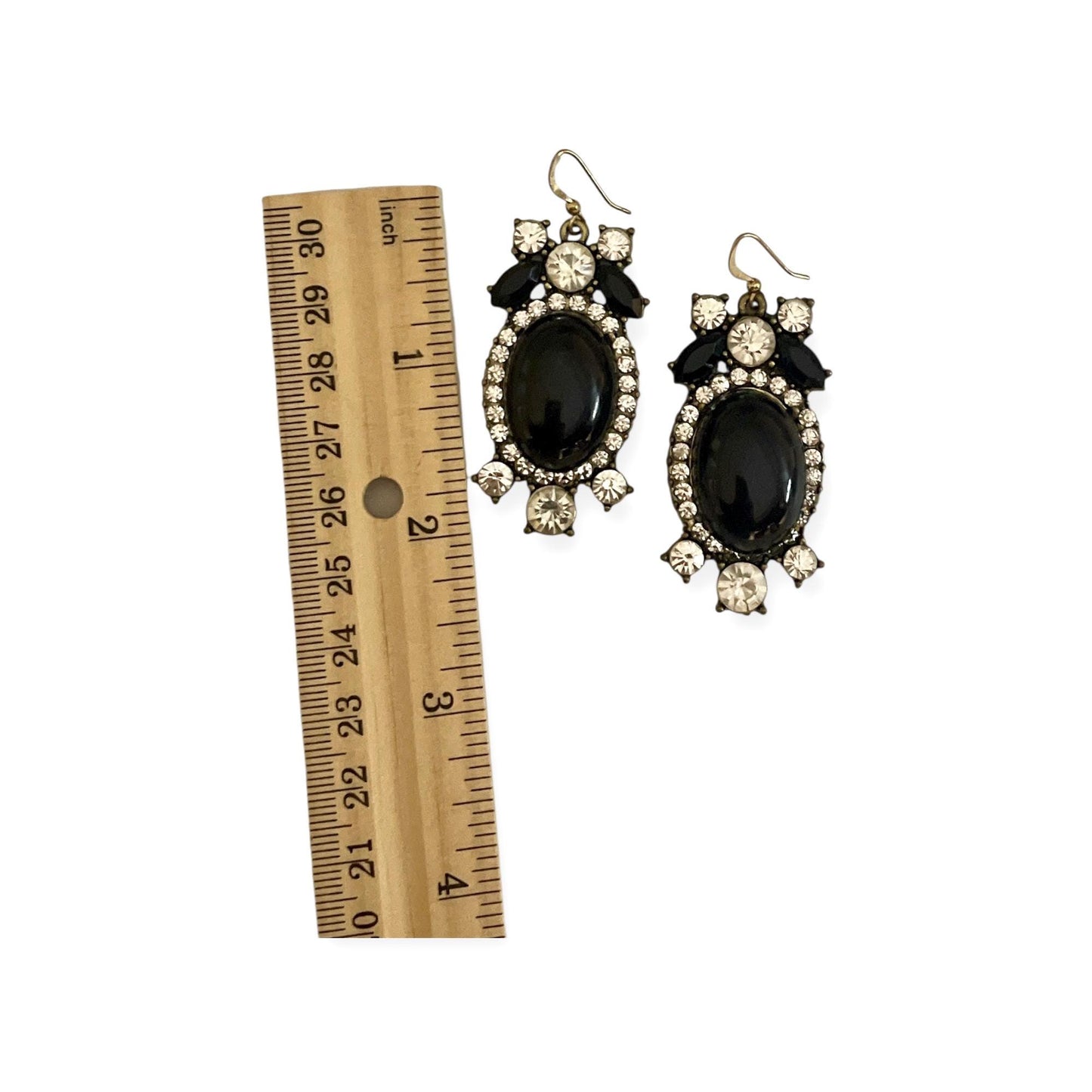 A pair of black and white earrings with rhinestones and a gold hook, placed next to a ruler for size comparison.