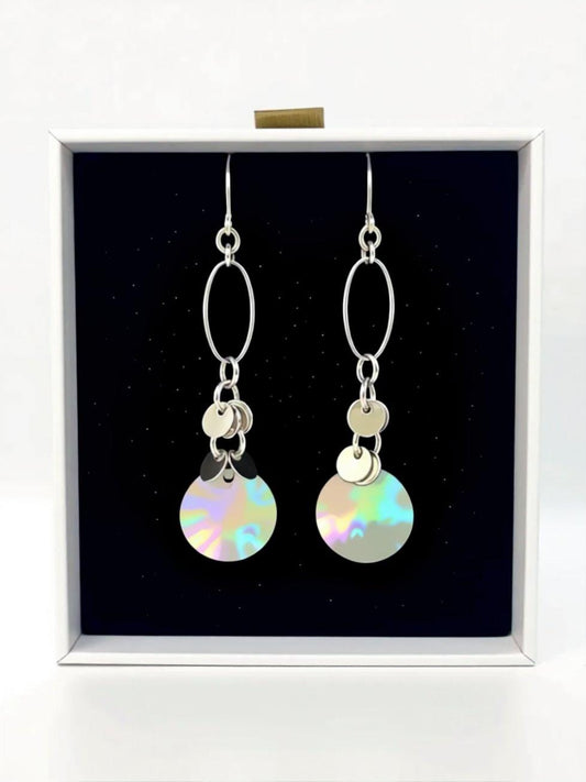 A pair of silver earrings with circular designs hanging from the ear hooks, displayed in a white box against a black background.