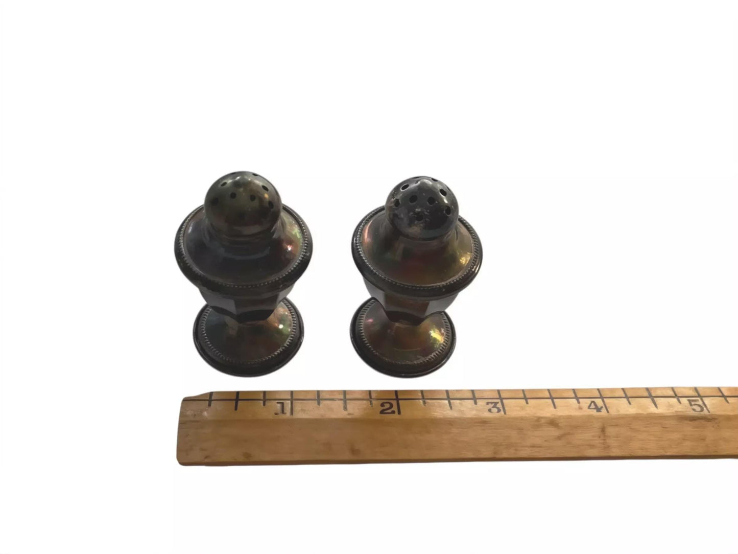two metal salt and pepper shakers placed next to a wooden ruler for size comparison.