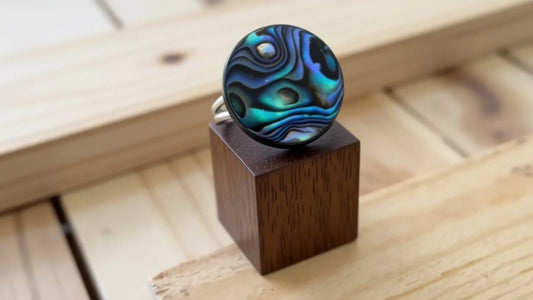 A wooden stand displays a ring with a blue and green abstract design on its surface.
