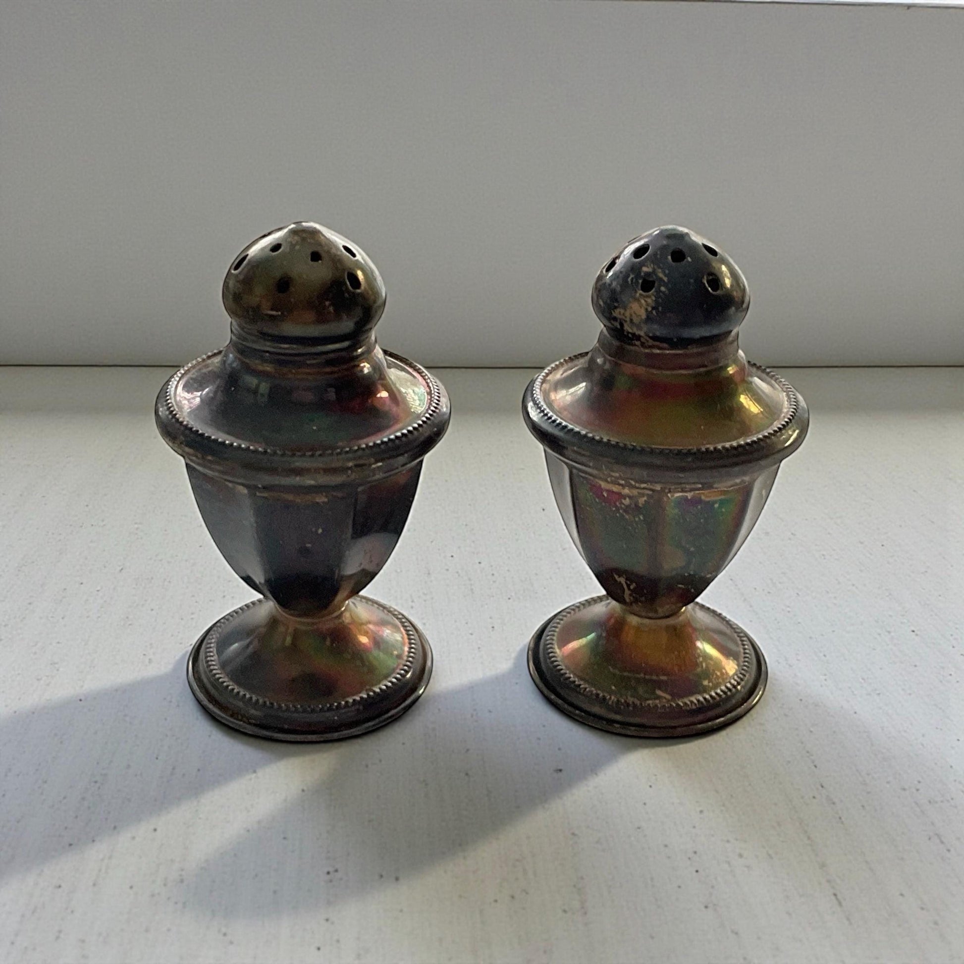 Two silver salt and pepper shakers are placed side by side on a white surface.