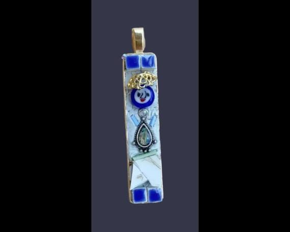 A colorful pendant with a mix of blue, white, and gold elements, including a small blue flower, a gold crown, and a silver teardrop-shaped charm.