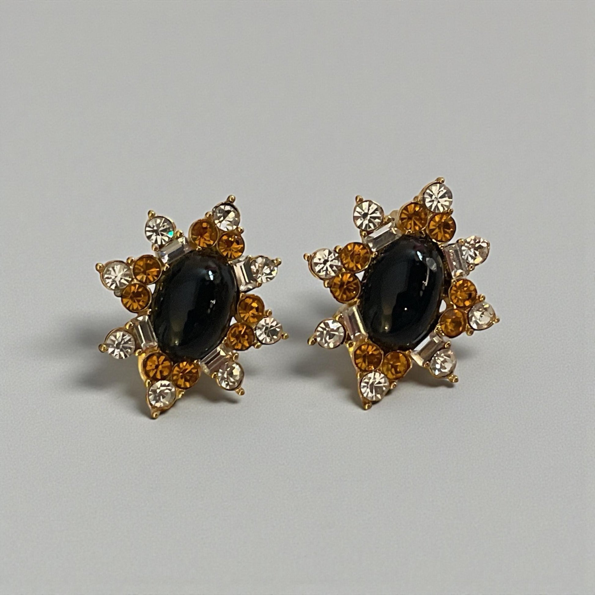 A pair of elegant earrings with a black gemstone surrounded by a star-shaped arrangement of smaller gemstones and gold accents.