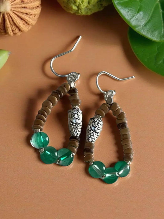 A pair of earrings with a combination of green beads and brown beads, featuring a silver owl charm.