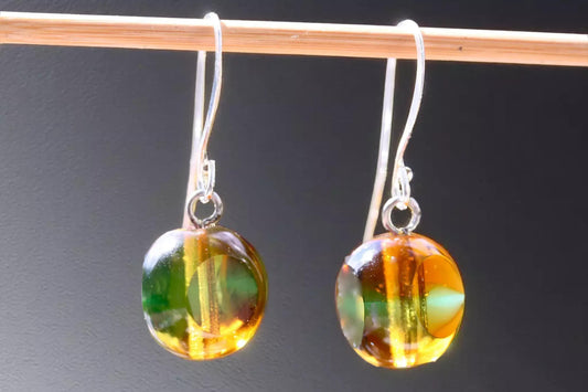 A pair of earrings with colorful glass beads hanging from a hook against a dark background.