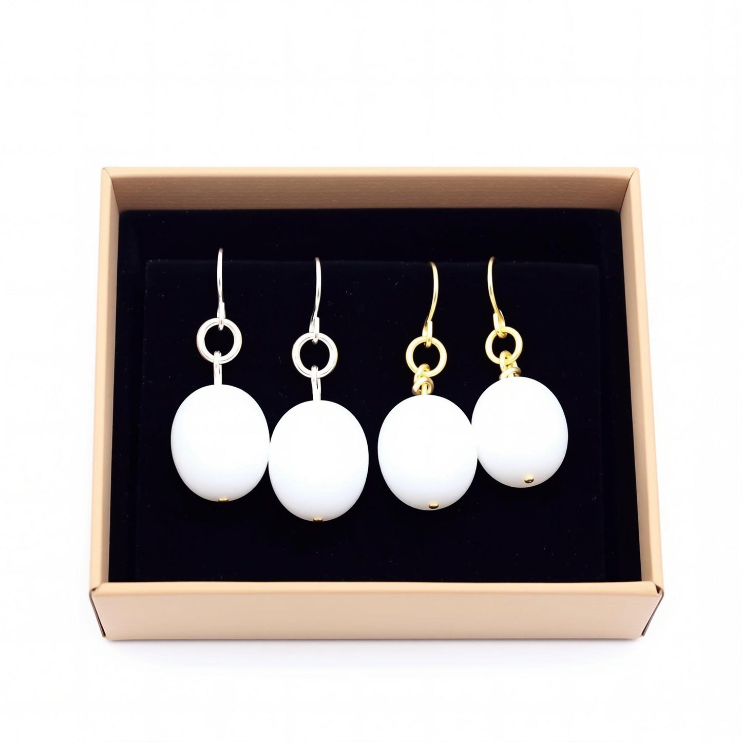 A pair of white pearl earrings with gold-colored hooks displayed in a beige jewelry box.