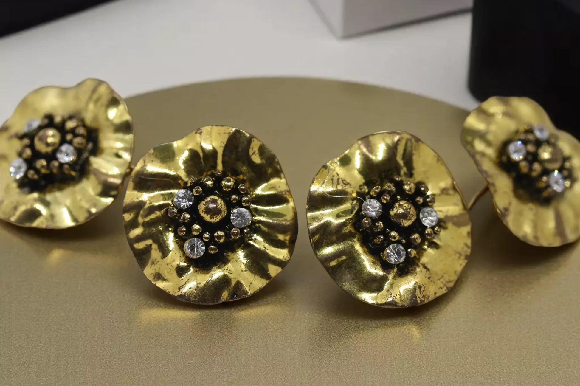 a pair of gold-colored earrings with black and white gemstones, arranged on a gold surface.
