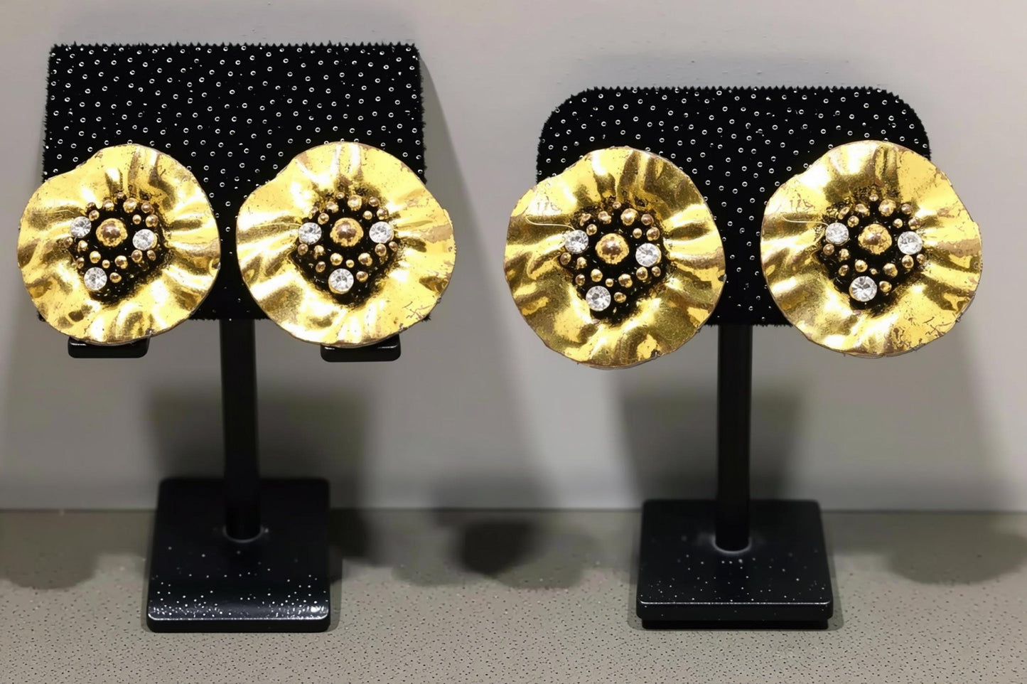a pair of gold-colored earrings with a floral design and small white stones or crystals as the centerpieces.
