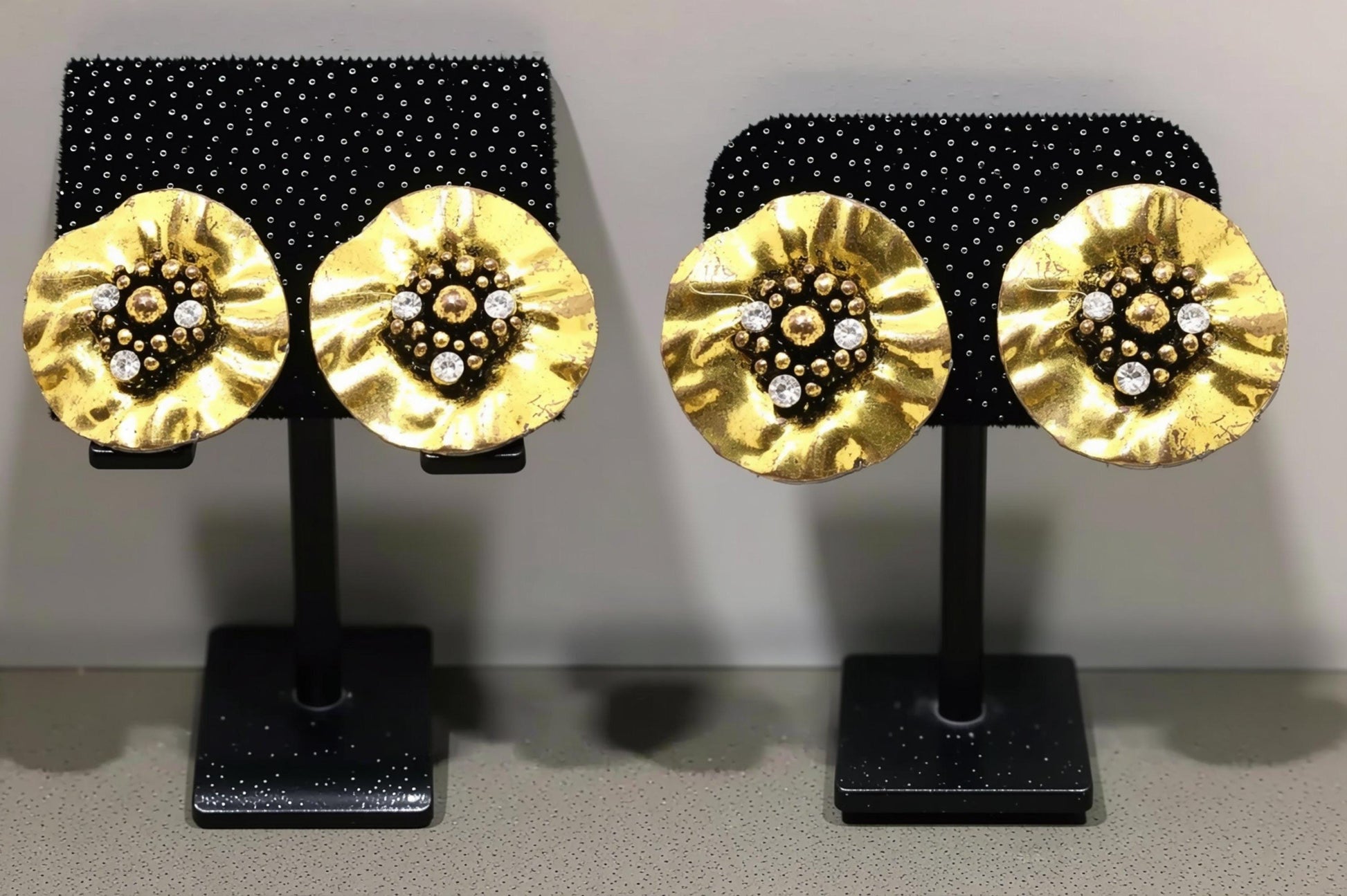 a pair of gold-colored earrings with a floral design and small white stones or crystals as the centerpieces.