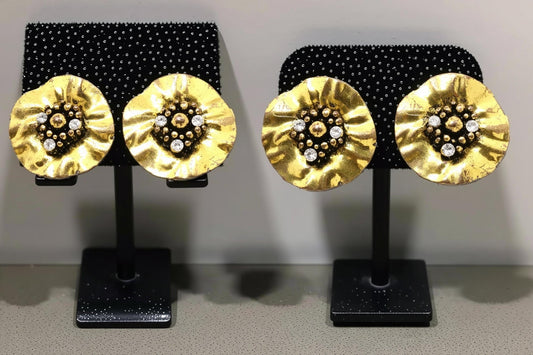 a pair of gold-colored earrings with a floral design and small white stones or crystals as the centerpieces.