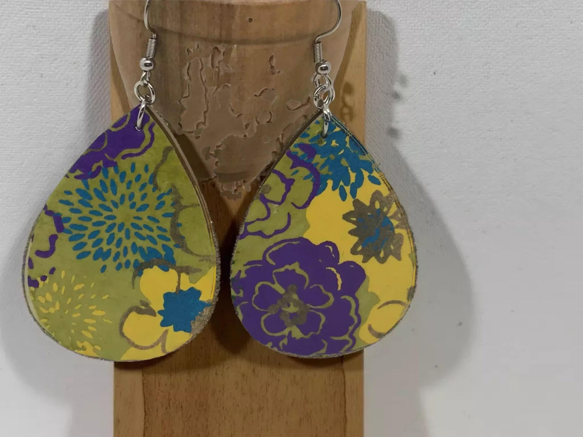 A pair of colorful earrings with floral designs, hanging from a hook against a plain background.