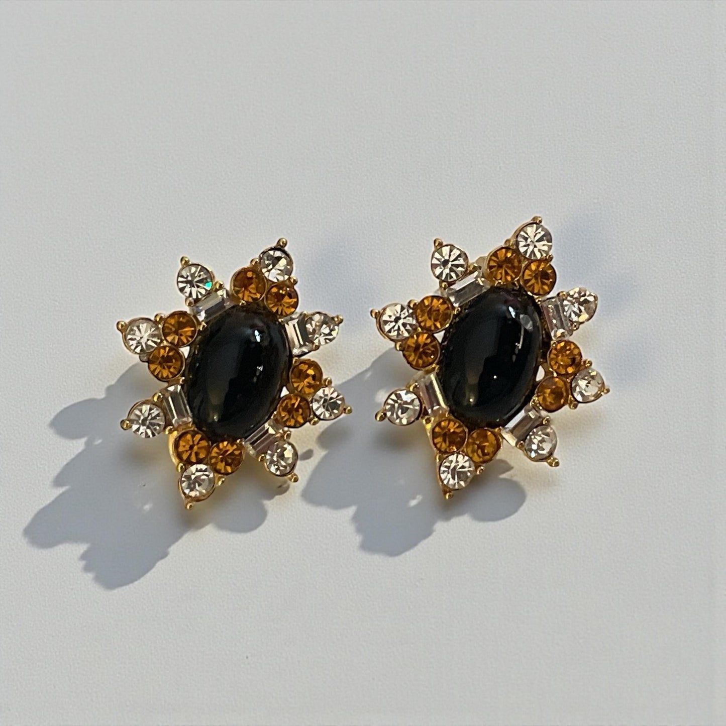 A pair of elegant earrings with a black gemstone surrounded by a star-shaped arrangement of smaller gemstones and gold accents.