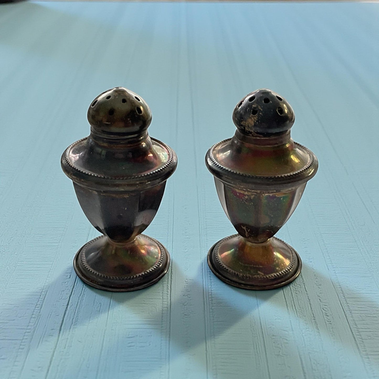 Two antique-looking metal salt and pepper shakers are placed side by side on a blue surface.