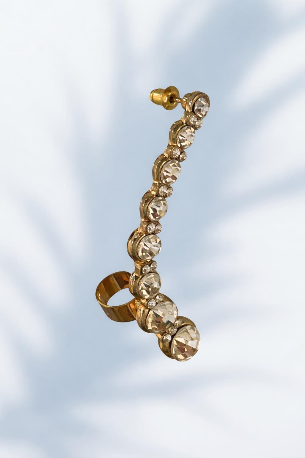 A gold earring with a row of small diamonds or gemstones attached to it, hanging against a light blue background.