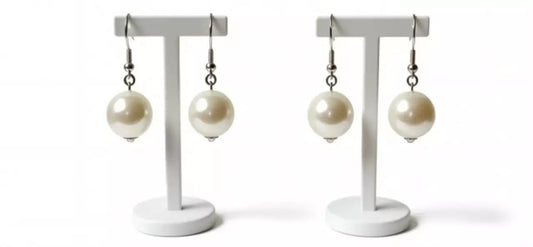 a pair of white earrings with large, round pearls hanging from hooks on a white stand.