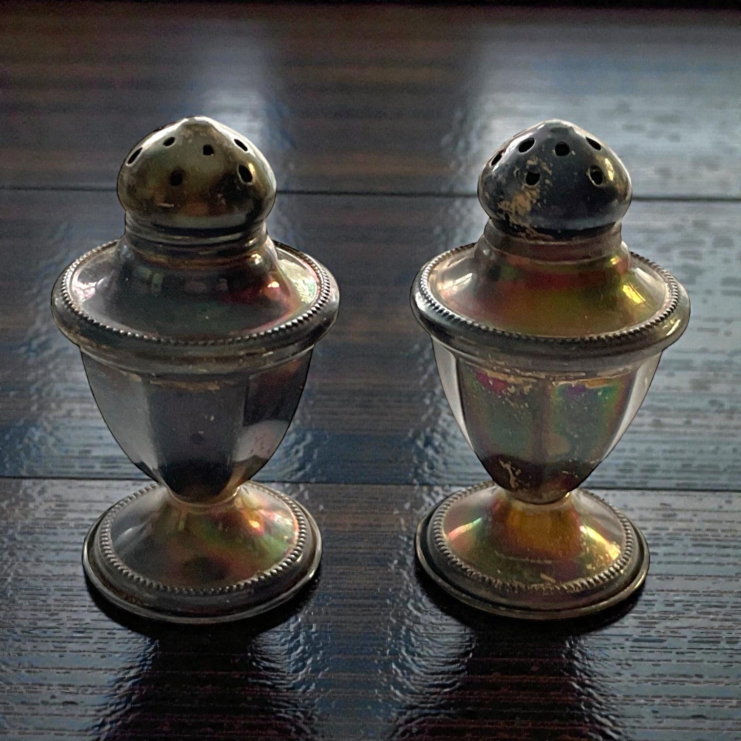 Two silver salt and pepper shakers with round tops and a reflective surface are placed on a wooden table.