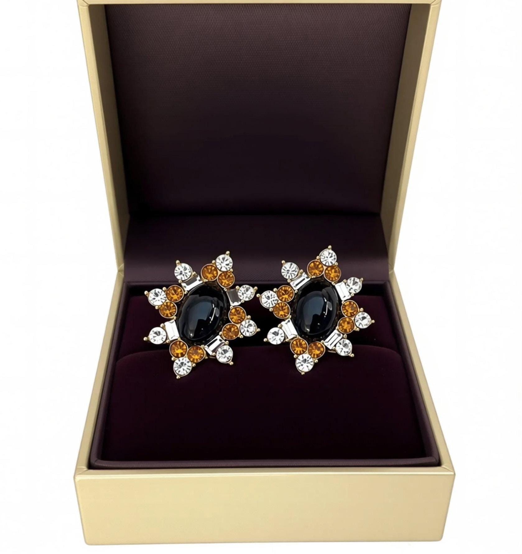A pair of earrings with a black oval stone surrounded by a floral design and small, round, and clear gemstones.