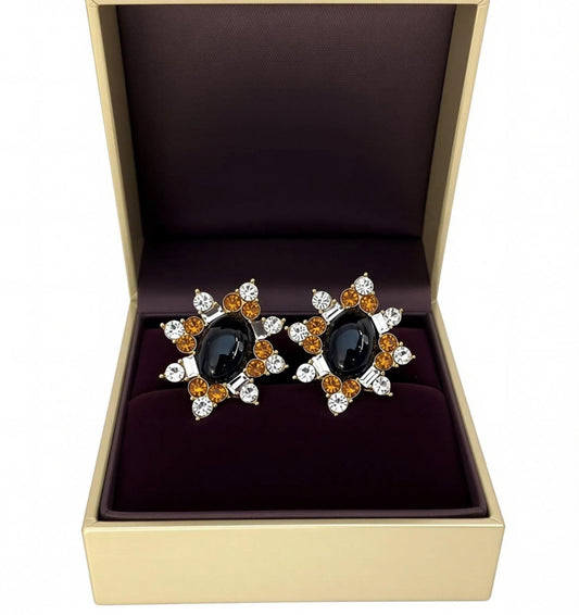 A pair of earrings with a black oval stone surrounded by a floral design and small, round, and clear gemstones.