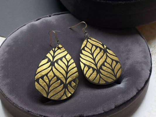 A pair of gold leaf earrings with a leaf pattern design, displayed on a gray velvet background.