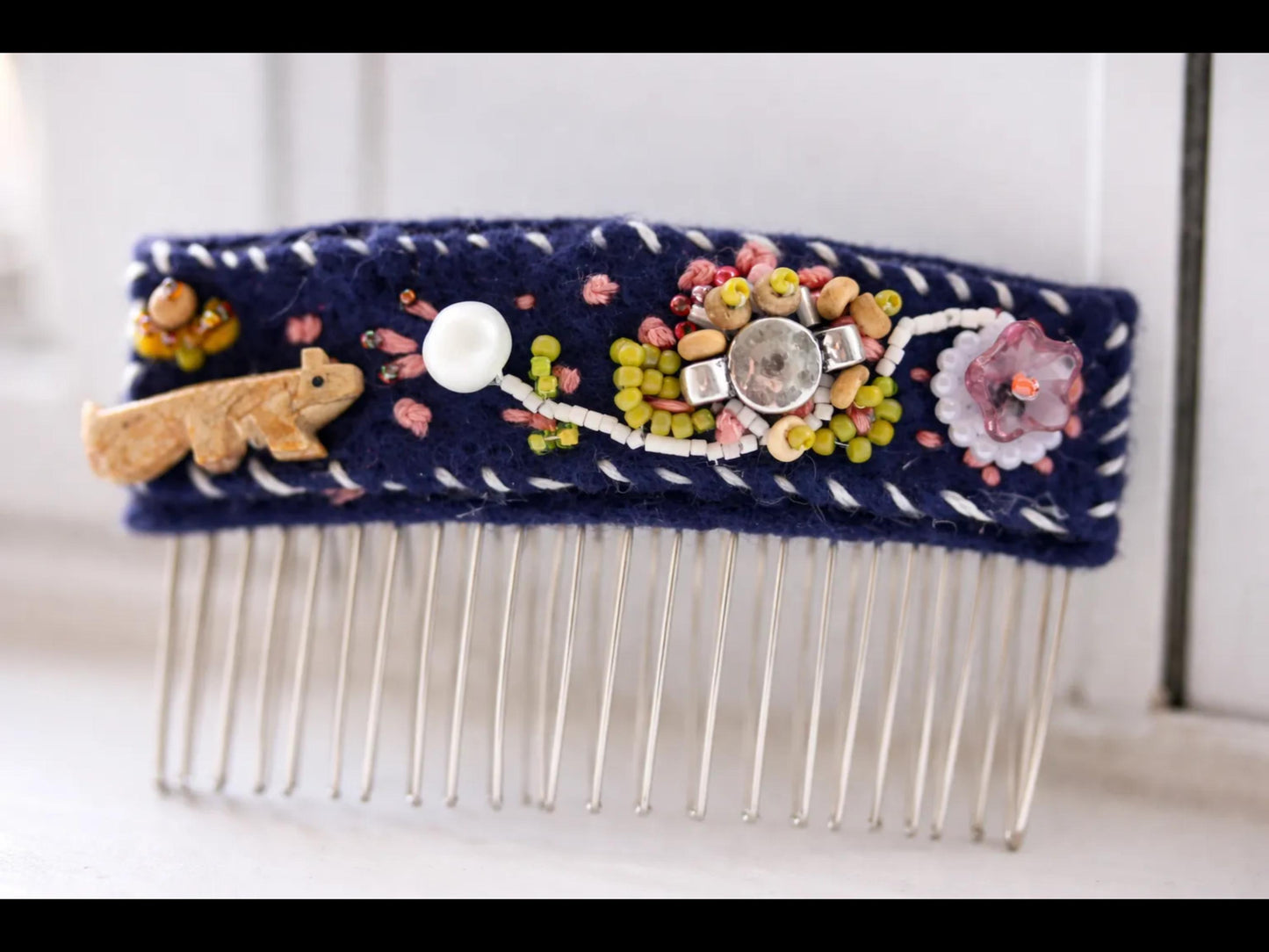 A close-up image of a decorative hair comb with various embellishments, including a small animal figurine, beads, and a large gemstone.
