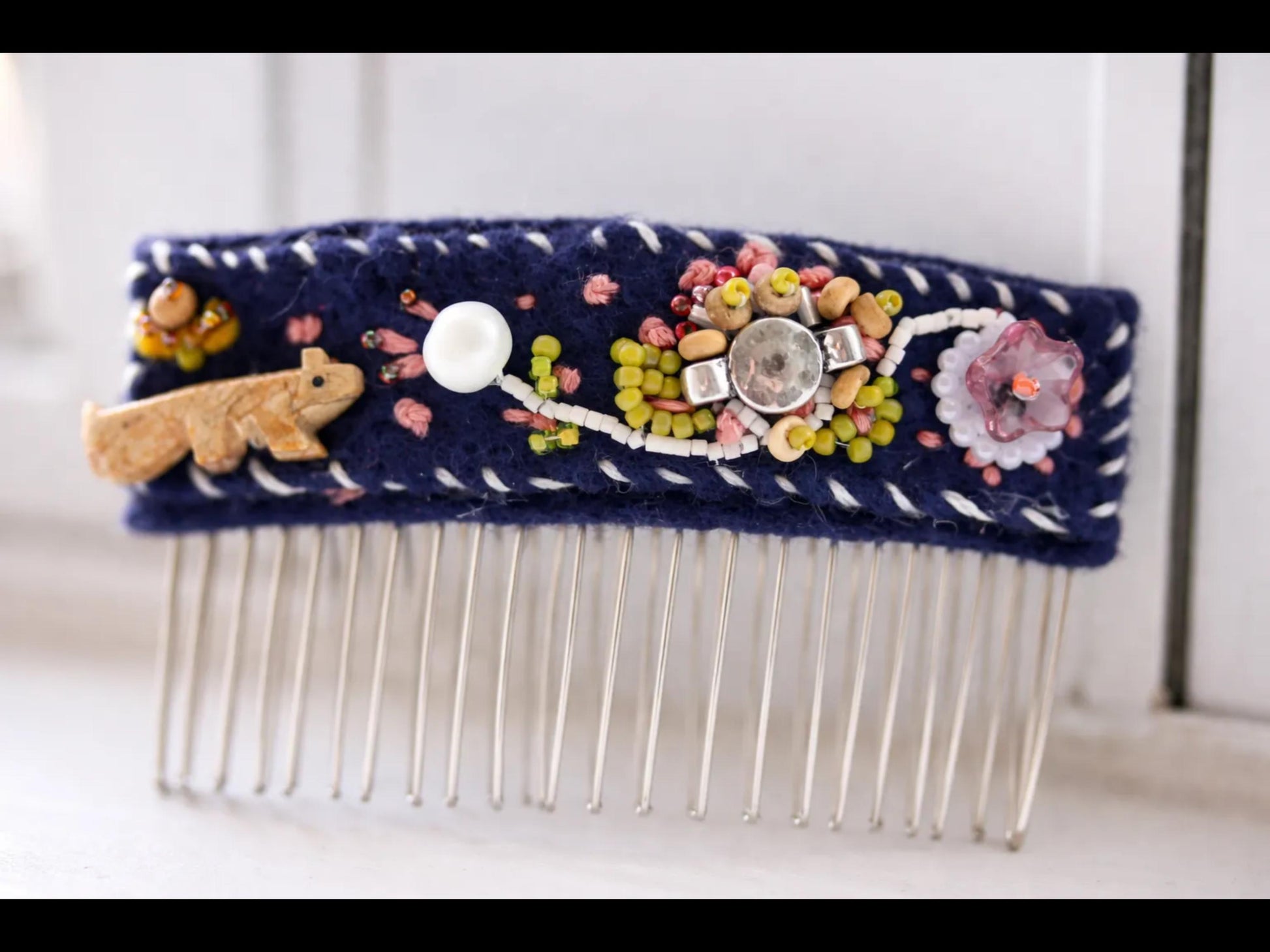 A close-up image of a decorative hair comb with various embellishments, including a small animal figurine, beads, and a large gemstone.