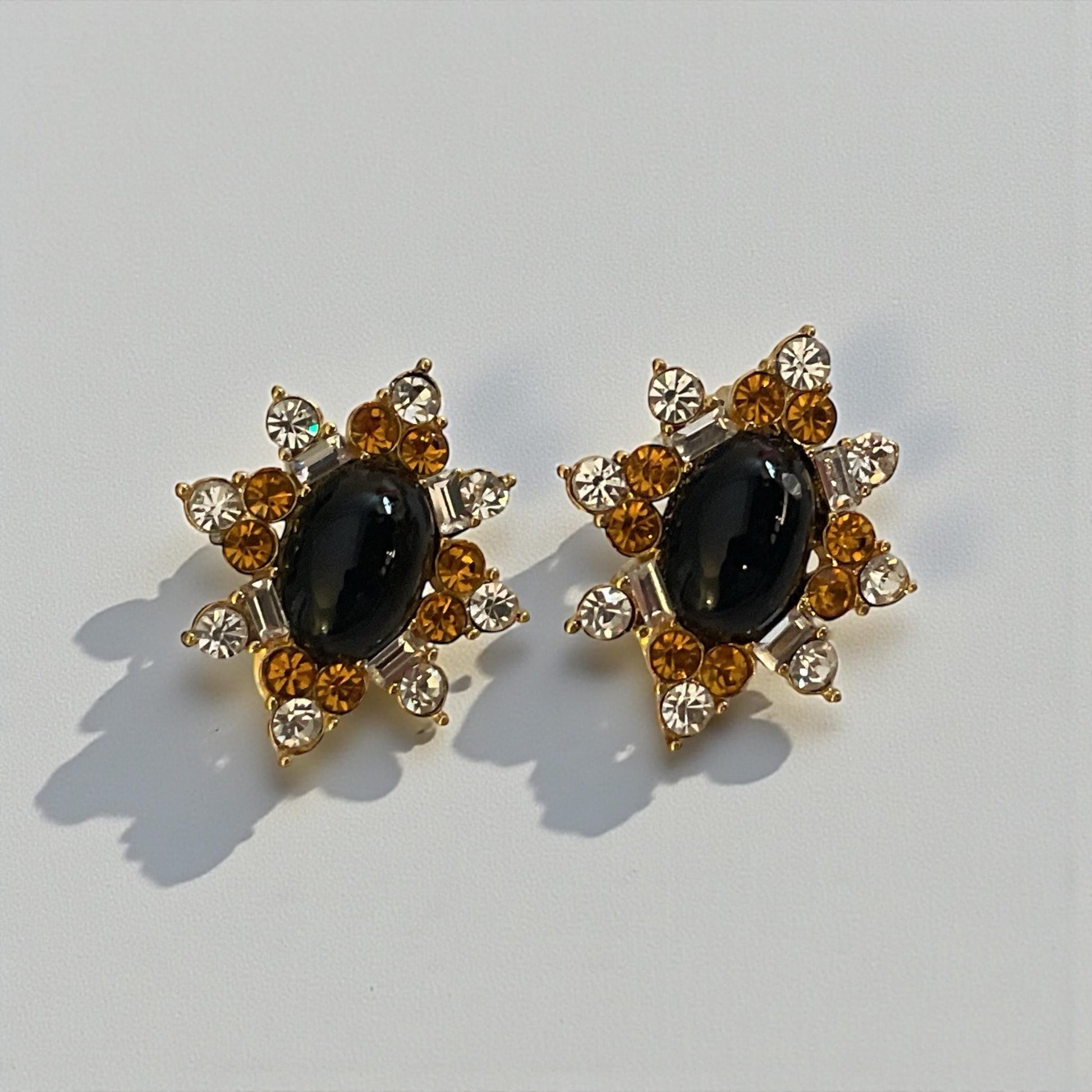 A pair of elegant earrings with a black gemstone surrounded by a star-shaped arrangement of smaller gemstones and gold accents.