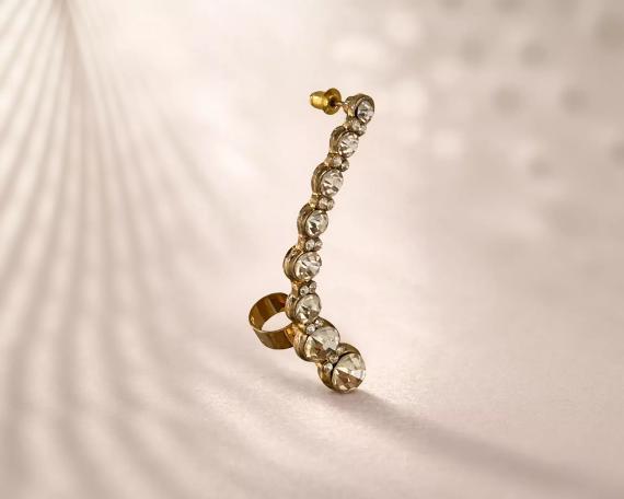 A gold earring with a row of clear gemstones, including diamonds, is shown against a light background.