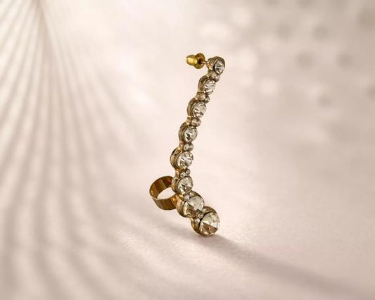 A gold earring with a row of clear gemstones, including diamonds, is shown against a light background.
